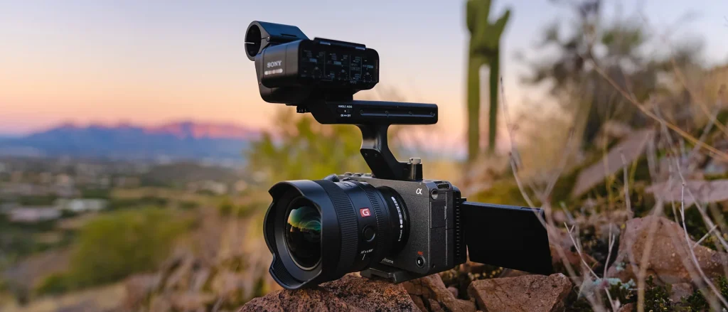 Камера Sony FX3 із широкекутним об'єктивом серії G та верхньою аудіоручкою з XLR-входами, закріплена на камені на тлі вечірнього пейзажу з кактусами.