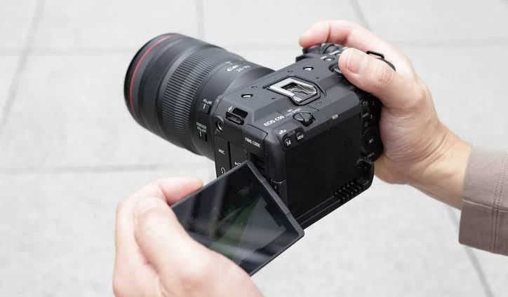 Кінокамера Canon EOS C50 з об'єктивом Canon RF на кахельній підлозі, оператор регулює відкидний сенсорний дисплей обома руками